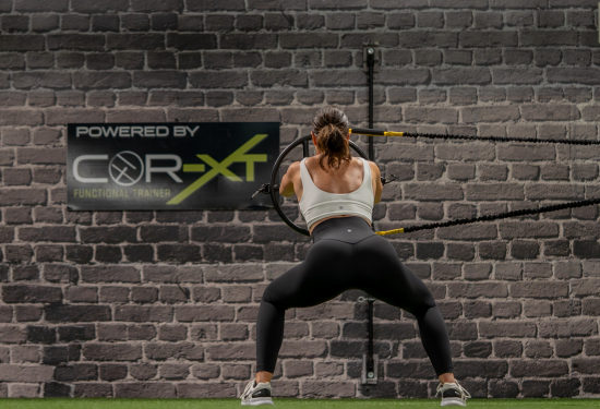 "COR-XT logo with a person using the functional trainer in the background."